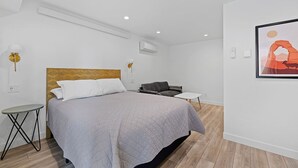 Moderni hotellihuone, jossa on suuri sänky, pieni sohva, sivupöytä ja seinällä oleva taulu.