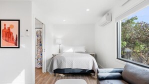 A modern bedroom with a bed, a sofa, a window with a view, and a door leading to another room. - Queen City Inn and Extended Stay #1 (Spearfish)