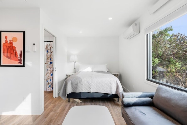 Un dormitorio moderno con cama, sofá, ventana con vistas y puerta que conduce a otra habitación.