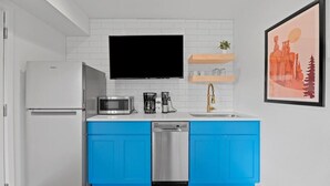 A modern kitchen with white appliances, blue cabinets, a mounted TV, and a coffee maker. - Queen City Inn and Extended Stay #1 (Spearfish)