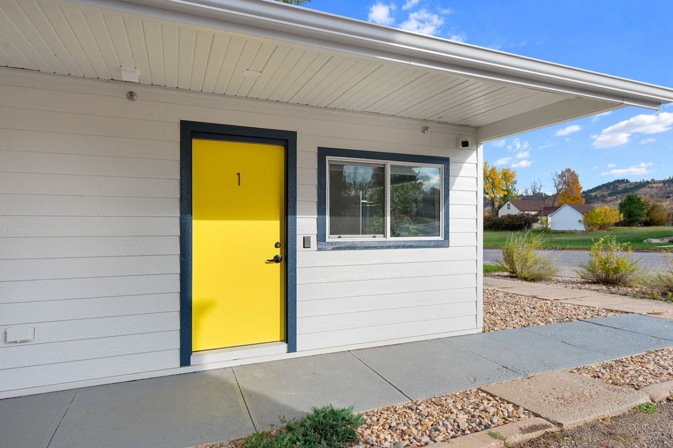 A single-story house with a yellow door, a window, and a covered porch.