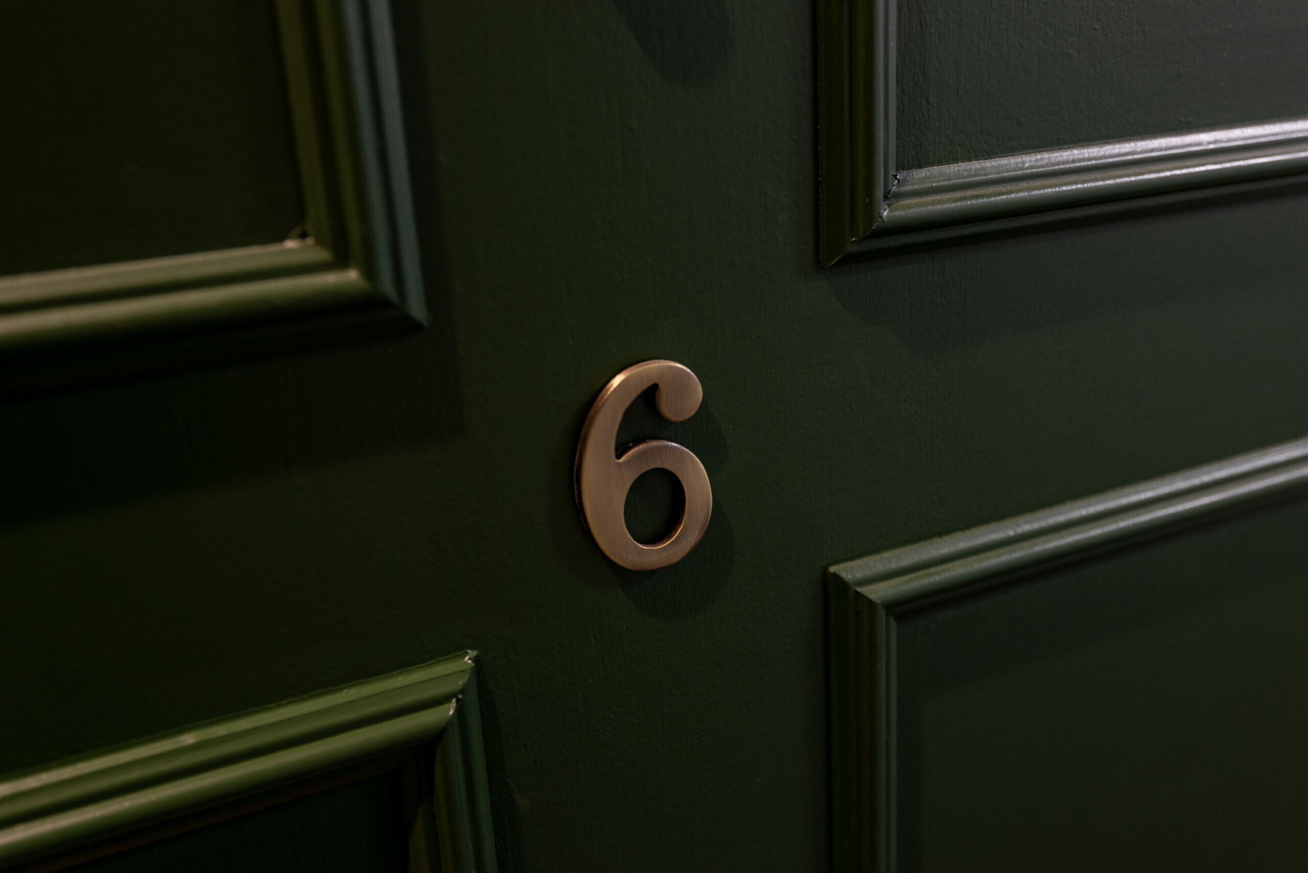 Primer plano de una puerta verde oscuro con una placa de latón con el número 6.