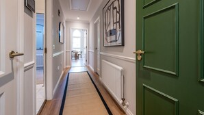 A hallway with a wooden floor, white walls, and green doors. There is a radiator on the right wall and a door with a number on it. - Skye Sands | St Mary’s Gardens (No 7) (St Andrews)
