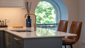 A modern kitchen with a white countertop, gold faucet, and a window with a view of greenery. - Skye Sands | St Mary’s Gardens (No 7) (St Andrews)