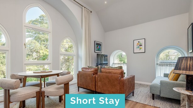A modern living room with a round table, sofas, and a TV. - Skye Sands | St Mary’s Gardens (No 7) (St Andrews)