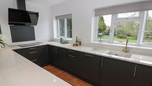 A modern kitchen with dark cabinets, white countertops, and a window providing a view of the outdoors. - Harran (Pershore)