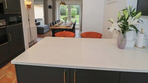 A modern kitchen with dark cabinets, a marble island, and orange chairs. - Harran (Pershore)