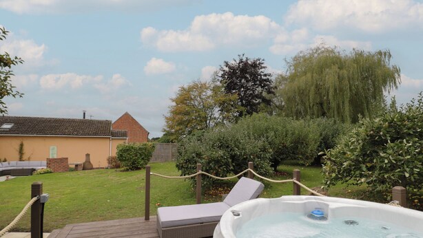 A hot tub on a wooden deck with a view of a house and trees. - Harran (Pershore)