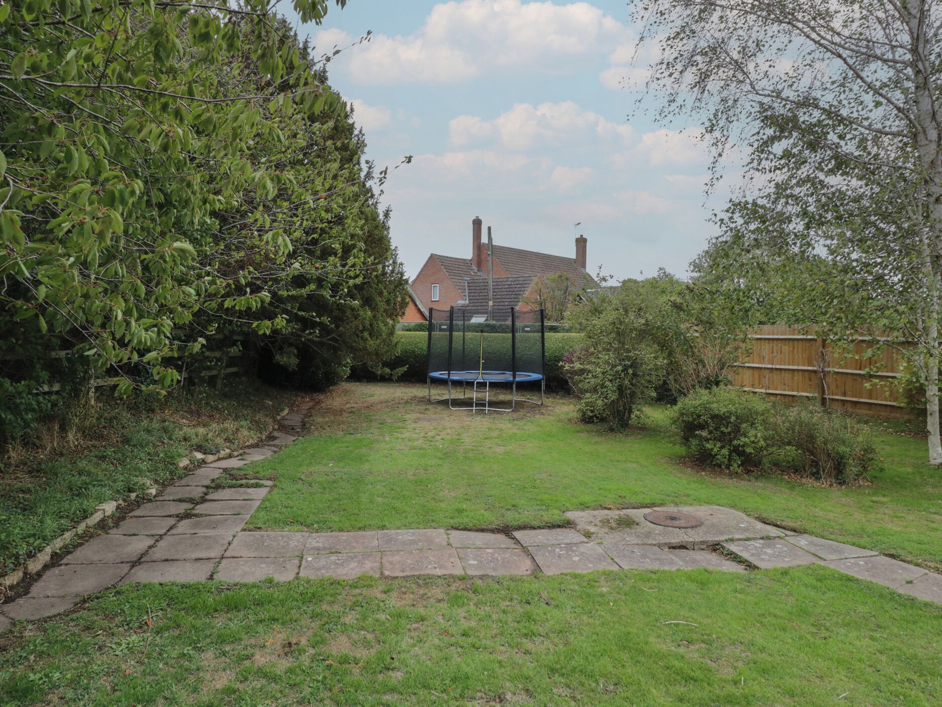 A backyard with a trampoline, a stone pathway, and a house in the background.