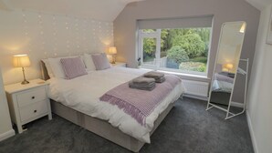 A bedroom with a bed, bedside lamps, a window with a view of greenery, and a full-length mirror. - Harran (Pershore)