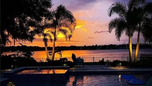 A sunset view from a poolside area with palm trees and a body of water in the background.