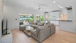 A spacious living area with a large sectional sofa, a glass coffee table, and a view of a pool and greenery through large sliding doors.