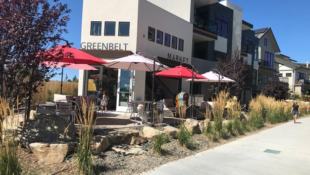 A modern building with a 'GREENBELT MARKET' sign, outdoor seating with umbrellas, and a paved walkway.
