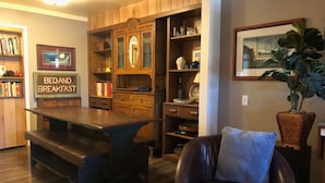 A cozy living room with a wooden dining table, a leather armchair, and a bookshelf.