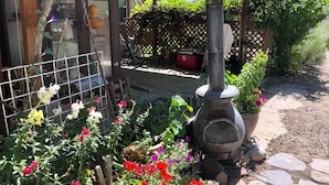 A rustic outdoor area with a wood-burning stove, a lattice fence, and a variety of flowering plants.