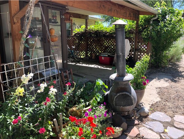A rustic outdoor area with a wood-burning stove, a lattice fence, and a variety of flowering plants.