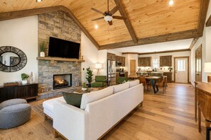 Ein geräumiges Wohnzimmer mit Kamin aus Stein, einem Flachbildfernseher, einer Couch und einem Essbereich mit Holzschränken.