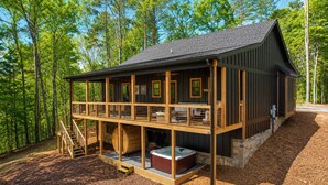 Een blokhut met een houten terras, een jacuzzi en een stenen fundering.