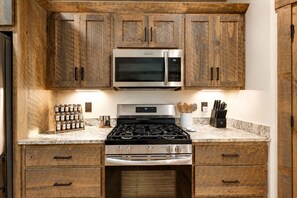 Una cucina con mobili in legno, un forno a microonde in acciaio inossidabile, un piano cottura a gas e un ripiano in marmo.