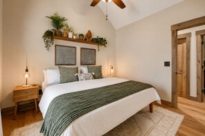 Ein Schlafzimmer mit einem Bett, Nachttischen, einem Deckenventilator, Wandregalen mit Pflanzen und zwei Wandbildern.