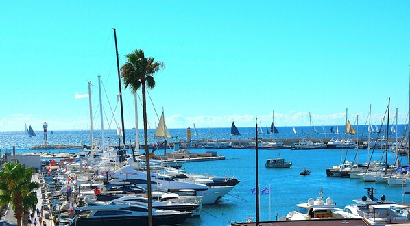 A marina with numerous boats docked, a lighthouse, and palm trees.