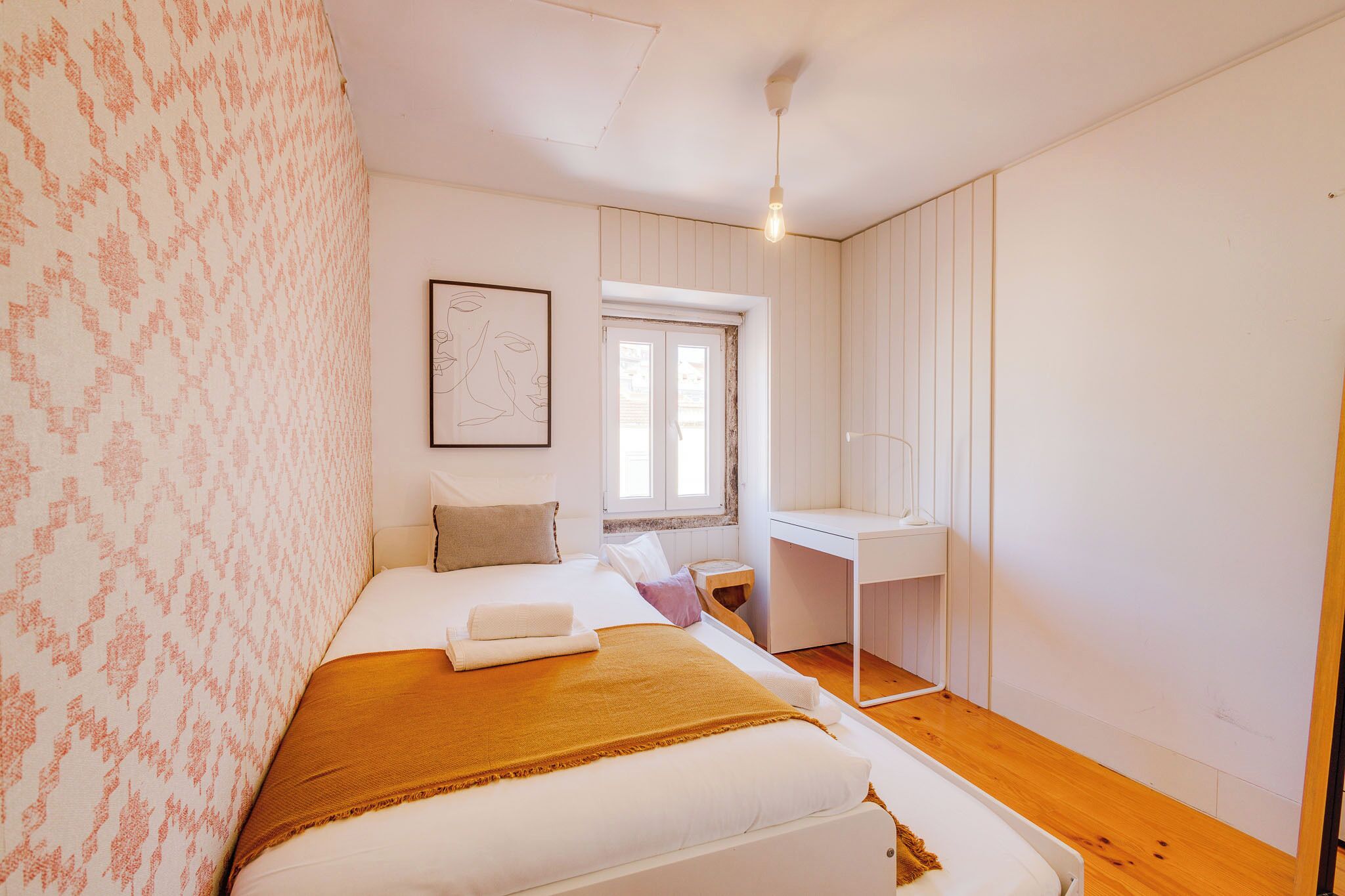 A bedroom with a bed, a desk, and a window.