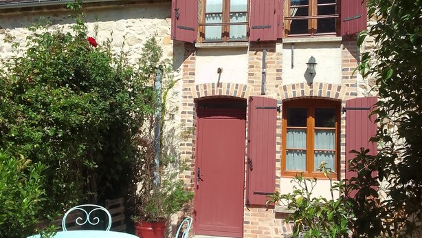 Un edificio de piedra de dos pisos, con contraventanas rojas y un pequeño ventanal circular en el techo.