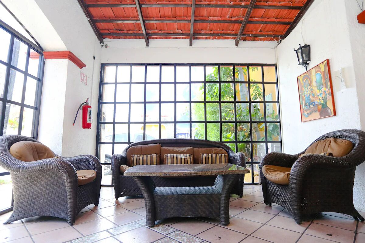 A room with wicker furniture, a tiled floor, and a large window with a view of greenery.