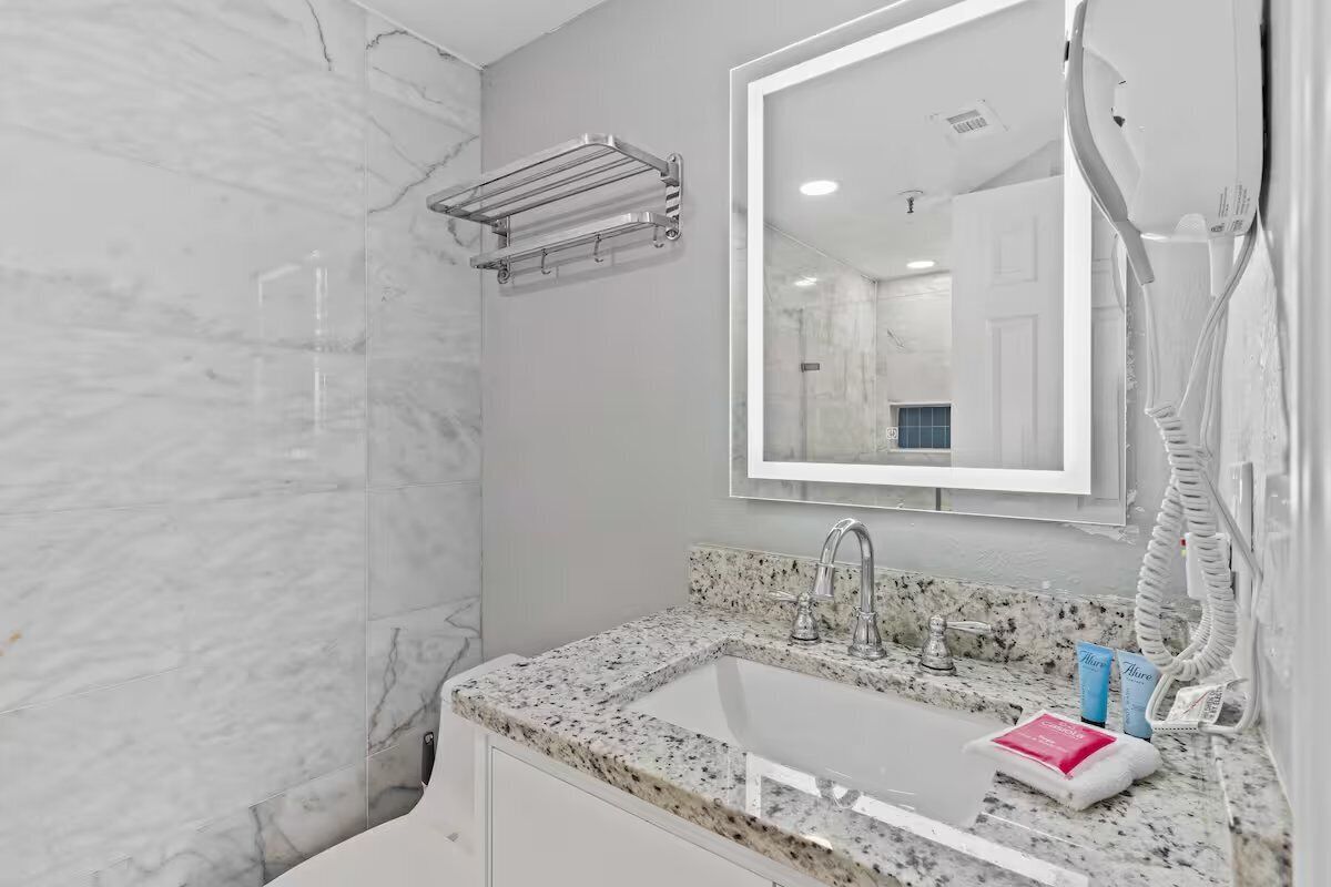A bathroom with a marble shower, a sink with a granite countertop, and a mirror above the sink.