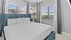 A modern hotel room with a large bed, a bedside table, a lamp, and a view of the city through the window. - Modern 2-Bedroom Enclave Condo Retreat (Orlando)