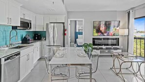 A modern kitchen with white cabinets, a built-in microwave, and a large TV mounted on the wall. - Modern 2-Bedroom Enclave Condo Retreat (Orlando)