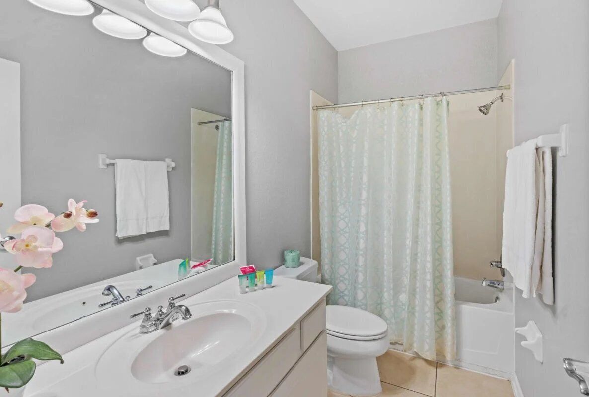A bathroom with a white sink, mirror, and toilet. There is a shower curtain and a towel rack.
