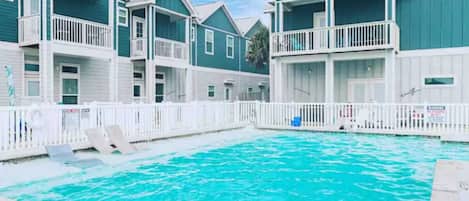 A swimming pool surrounded by multi-story buildings with balconies, a white fence, and a 'NO DIVING' sign.