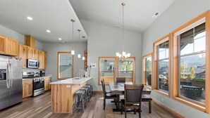 A modern kitchen with wooden cabinets, stainless steel appliances, and large windows offering a view of the outdoors.