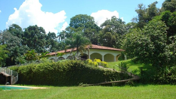 A building with a tiled roof, surrounded by lush greenery and a swimming pool. - Charming place, with a cozy single-story house. (Mairinque)