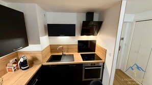 Una cocina compacta con encimera negra, electrodomésticos de acero inoxidable y horno empotrado.