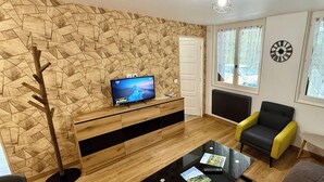 Una sala de estar moderna con un diseño geométrico en la pared, un televisor de pantalla plana, un sofá, una mesa de centro y un sillón.
