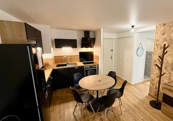A compact kitchen with a dining area, a built-in oven, and a modern stove. - Le Bélouga 4 Le Mont Dore (Mont-Dore)