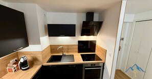 A compact kitchen with a black countertop, stainless steel appliances, and a built-in oven. - Le Bélouga 4 Le Mont Dore (Mont-Dore)