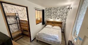A compact bedroom with a bunk bed, a single bed, a wooden headboard, a wall-mounted shelf, and a window with curtains. - Le Bélouga 4 Le Mont Dore (Mont-Dore)