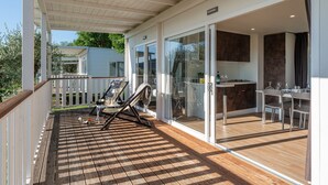 Una terraza cubierta al aire libre con piso de madera, una silla de descanso y una zona de comedor con mesa y sillas.