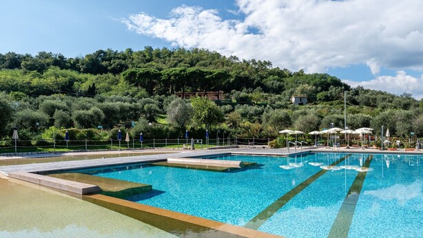 A clear swimming pool with steps leading into it, surrounded by a fence and umbrellas. - Mobile Home 'Camping Belsito Evo Medium 507' with Shared Pool, Wi-Fi & Air Conditioning (Vico)