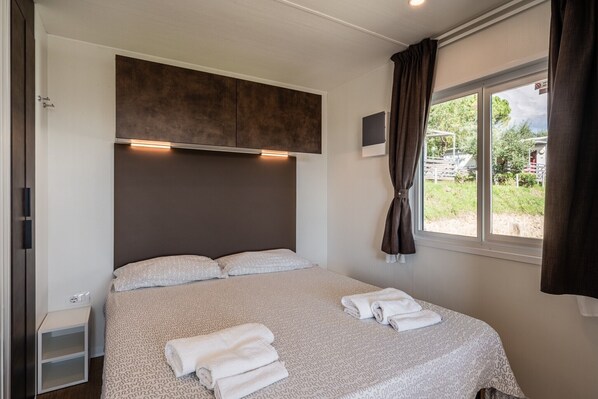 Un dormitorio con cama, una mesita de noche, una ventana con cortinas y vistas al exterior.