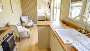 Cocina compacta con encimera de madera, un lavamanos y una zona de comedor con sillas.