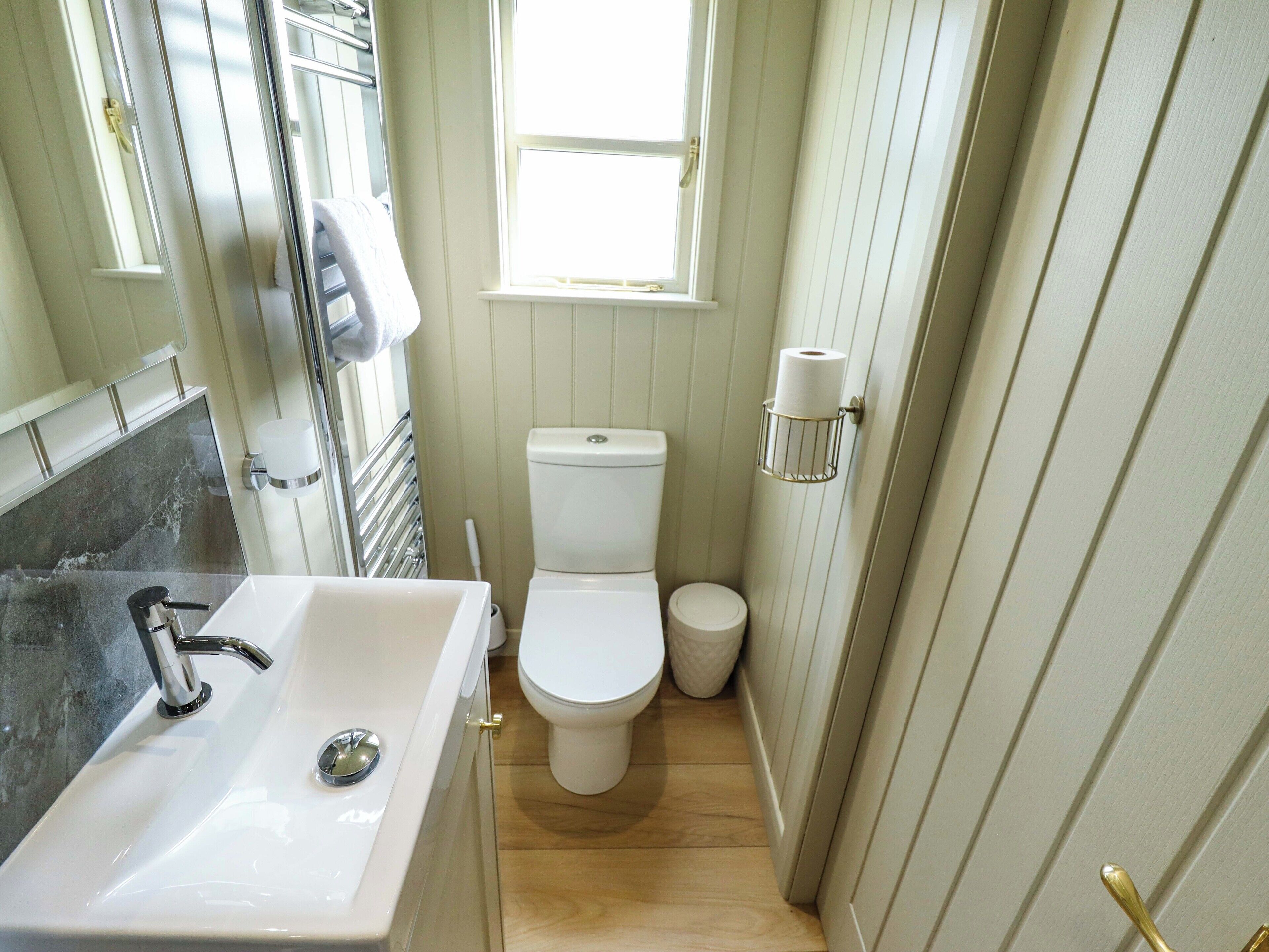 A small, clean bathroom with a white sink, a toilet, and a window.