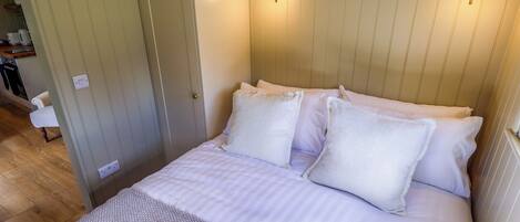 A neatly made bed with white linens and pillows, a rolled towel on the side, and a framed picture of shells on the wall.