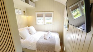 Una cama individual con sábanas blancas, una lámpara de noche y una ventana con persianas.