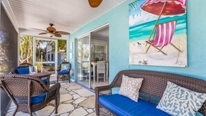 A covered patio with wicker furniture, a blue sofa, and a beach-themed painting. - Mermaid’s Purse~Private Pool! 40 steps to beach! (Anna Maria)