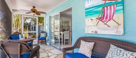 A covered patio with wicker furniture, a blue sofa, and a beach-themed painting.