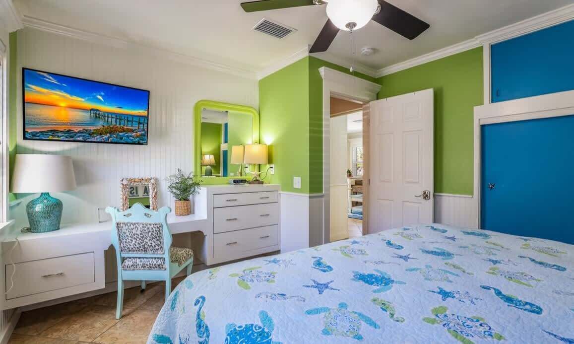 A bedroom with a bed, a desk, a chair, a TV, and a door.